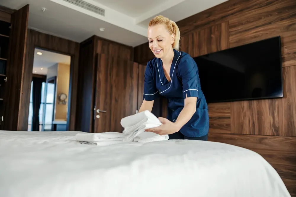 Addetta alle pulizie che sistema asciugamani puliti sul letto di una camera d'albergo
